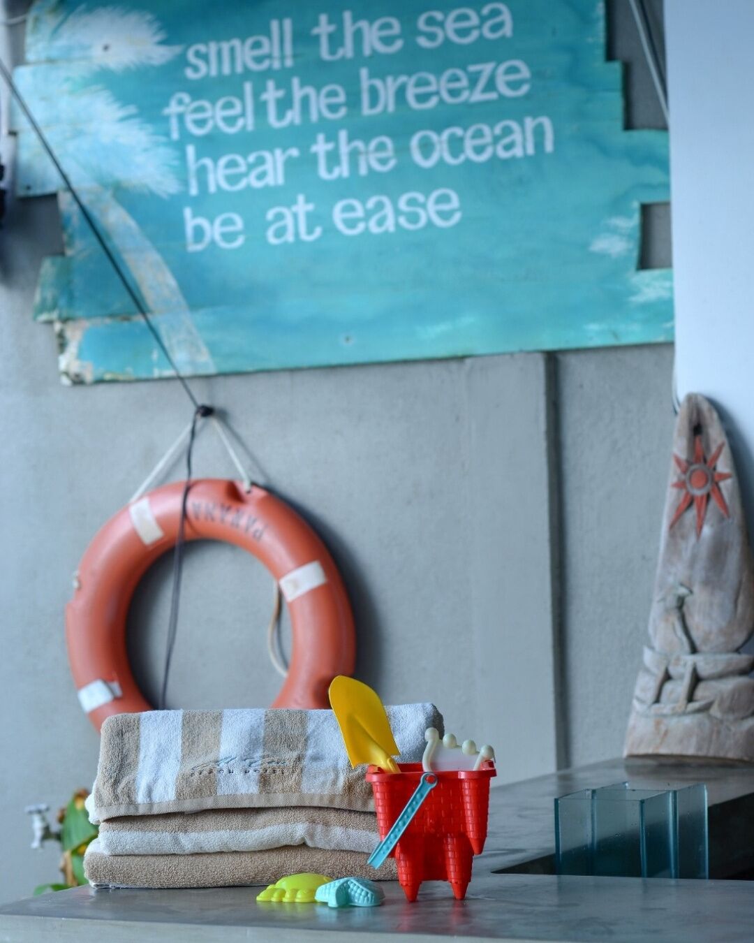Una habitación con un flotador, una toalla de playa, una pala de juguete y un cubo en un estante.