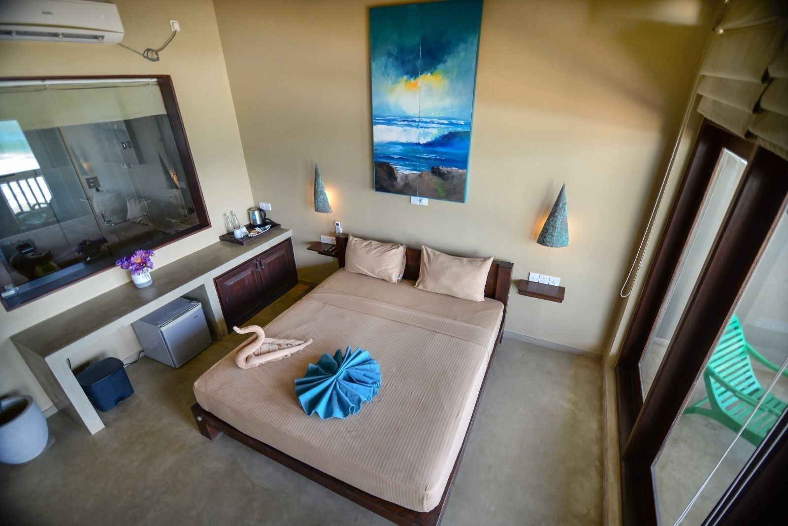 A hotel room with a bed, a desk, a mirror, a painting, and a window.