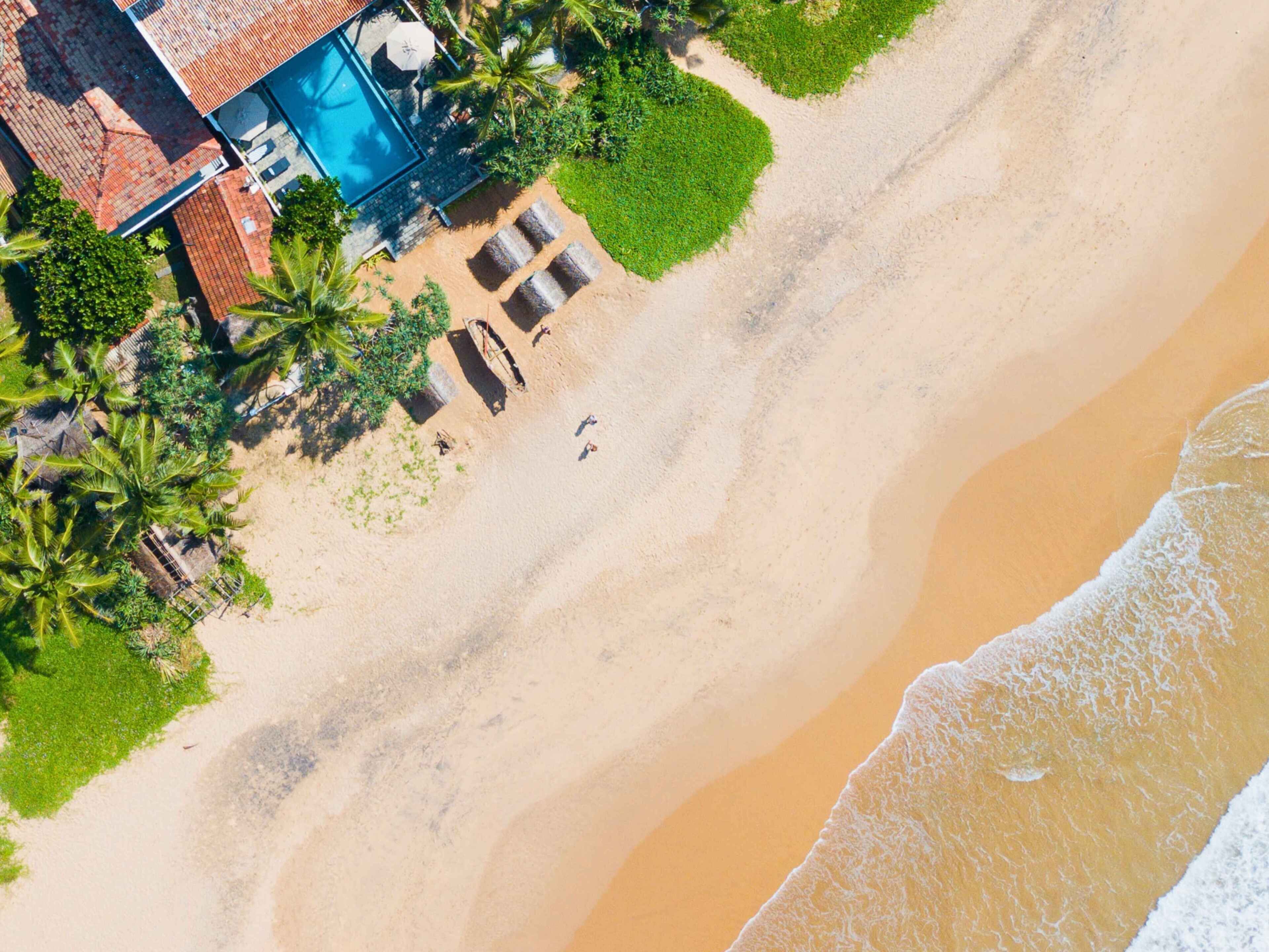 An aerial view of a beachside property with a swimming pool, lounge chairs, and a small boat.