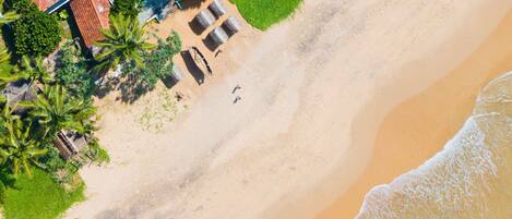 An aerial view of a beachside property with a swimming pool, lounge chairs, and a small boat.