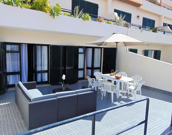 Relax in this serene outdoor seating area with a table, umbrella, and comfortable wicker sofa.