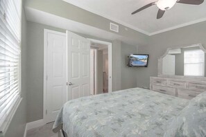 Ein Schlafzimmer mit Bett, Kommode, Deckenventilator und Fernseher an der Wand.