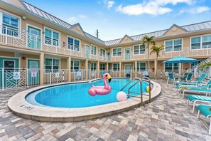 A hotel pool area with a swimming pool, lounge chairs, and a flamingo float. - Stunning Beach Suite, Heated Pool, Steps to Sand! Clearwater ➠ Beach Suites #105 (Clearwater Beach)
