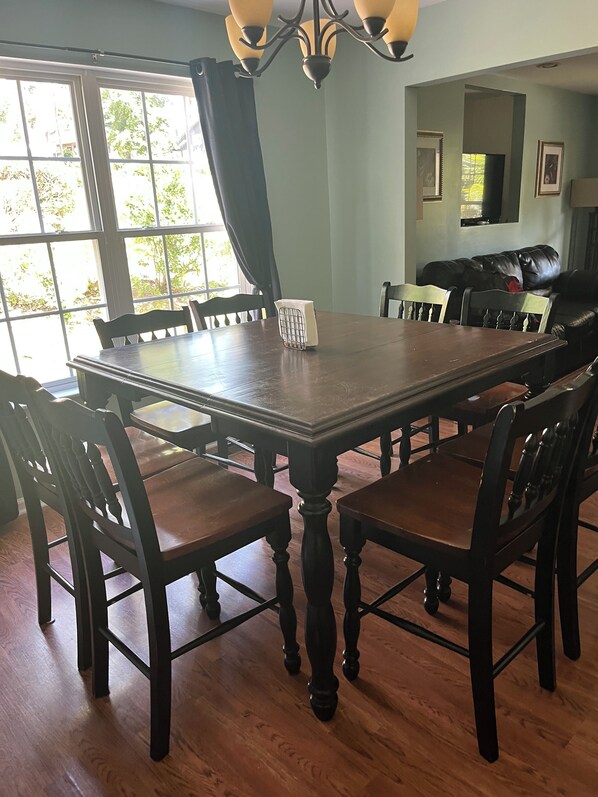 Un comedor con una amplia mesa y sillas de madera, un candelabro y vistas al exterior a través de grandes ventanales.