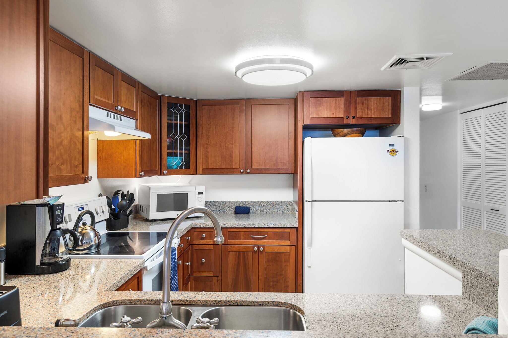 A kitchen with wooden cabinets, a stainless steel sink, a microwave, and a refrigerator.