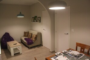 Ein Wohnzimmer mit einer Couch, einem kleinen Tisch und einem Esstisch für vier Personen.
