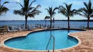 Una piscina con borde curvo, rodeada de palmeras y vista al mar.