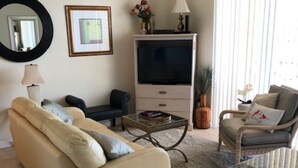 Una sala de estar con un sofá color crema, una mesa de centro, un mueble para televisión y un ventilador de techo.