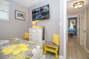 A bedroom with a bed, a dresser, a bench, and a television on the wall.