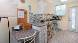 A compact kitchen with white cabinets, a granite countertop, a small island, and a window with blinds. - Cute beach condo with heated pool, steps to the sand ➠ CBS 204 (Clearwater)
