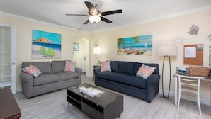 A living room with two sofas, a coffee table, and a ceiling fan. - Cute beach condo with heated pool, steps to the sand ➠ CBS 204 (Clearwater)