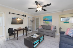 A living room with a ceiling fan, a coffee table, a sofa, and a TV mounted on the wall.