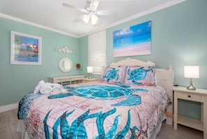 A bedroom with a bed, a ceiling fan, a nightstand, a lamp, and artwork on the walls.
