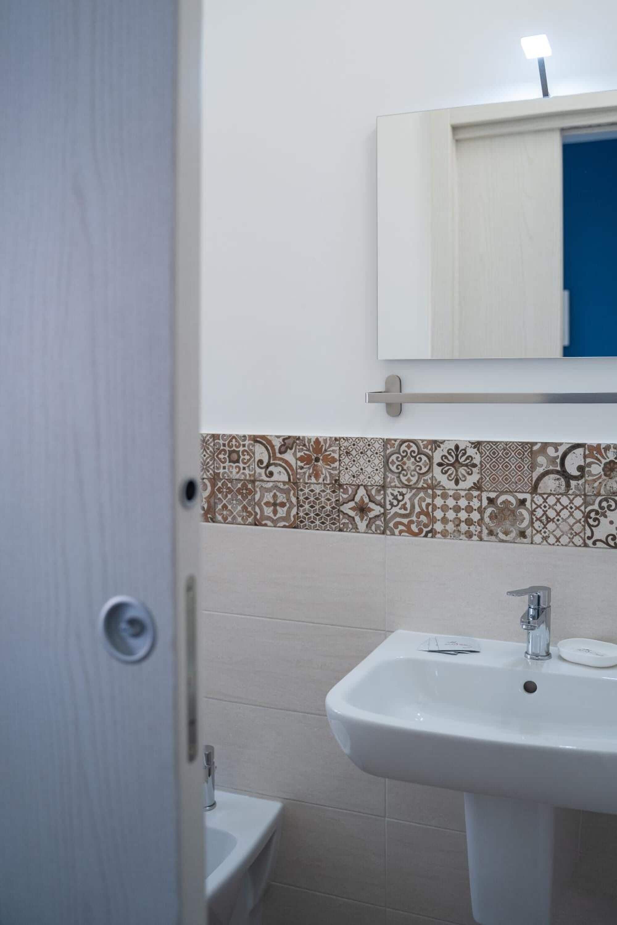 A bathroom with a white sink, a mirror above it, and a patterned tile backsplash.