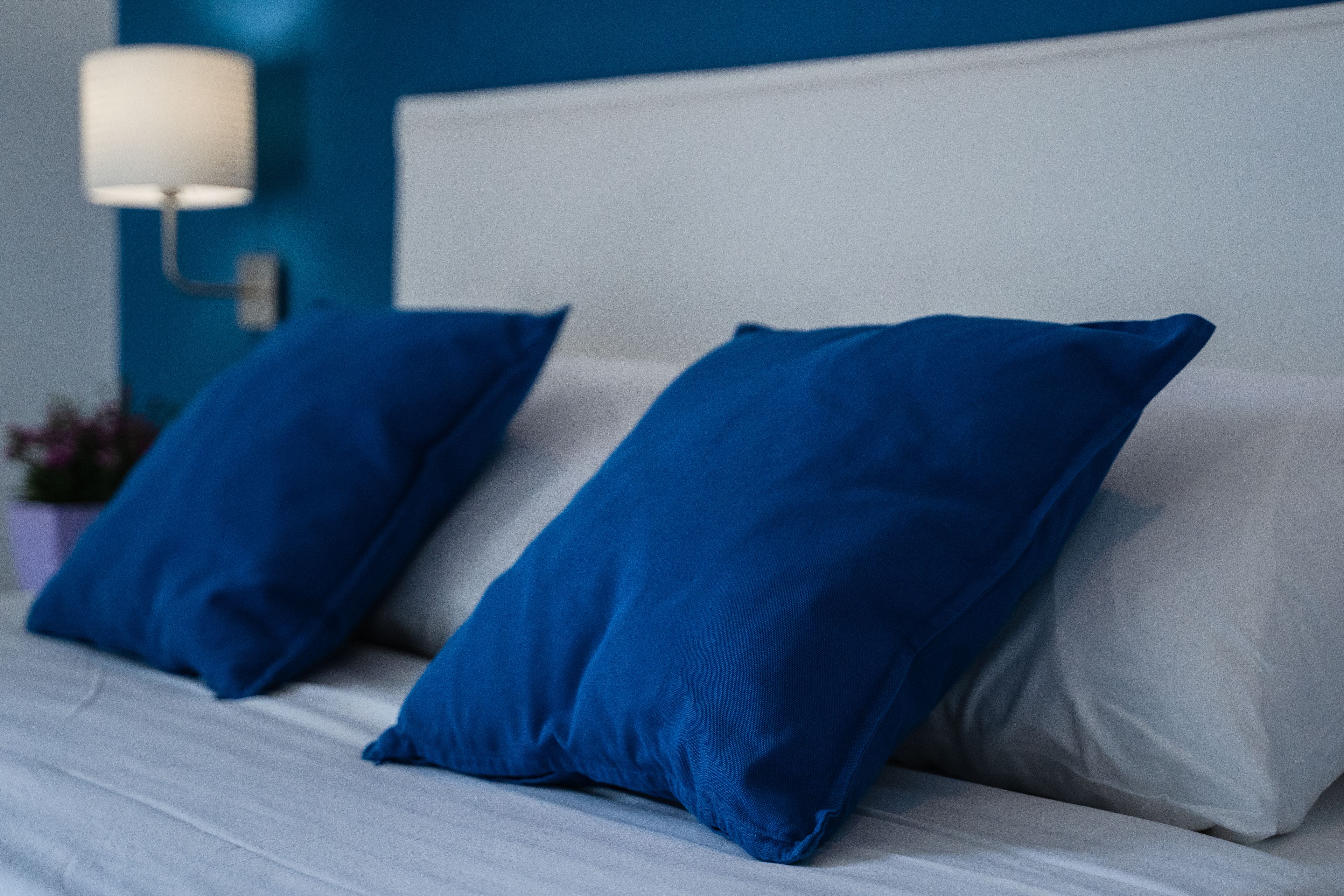 A bed with blue and white pillows, a white headboard, and a wall-mounted lamp.