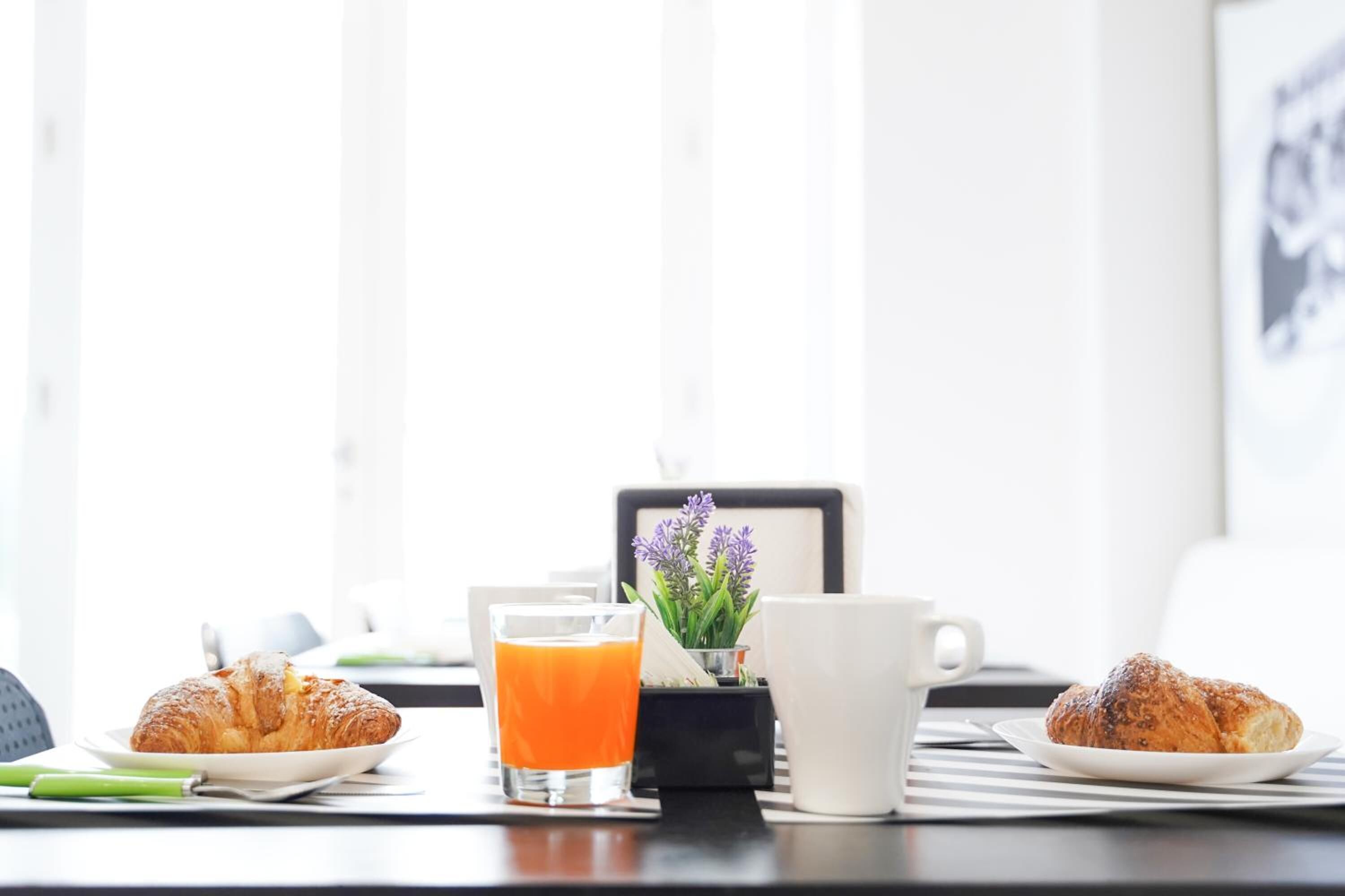 Una mesa con cruasanes, un vaso de zumo de naranja y una taza de café sobre un mantel con rayas.