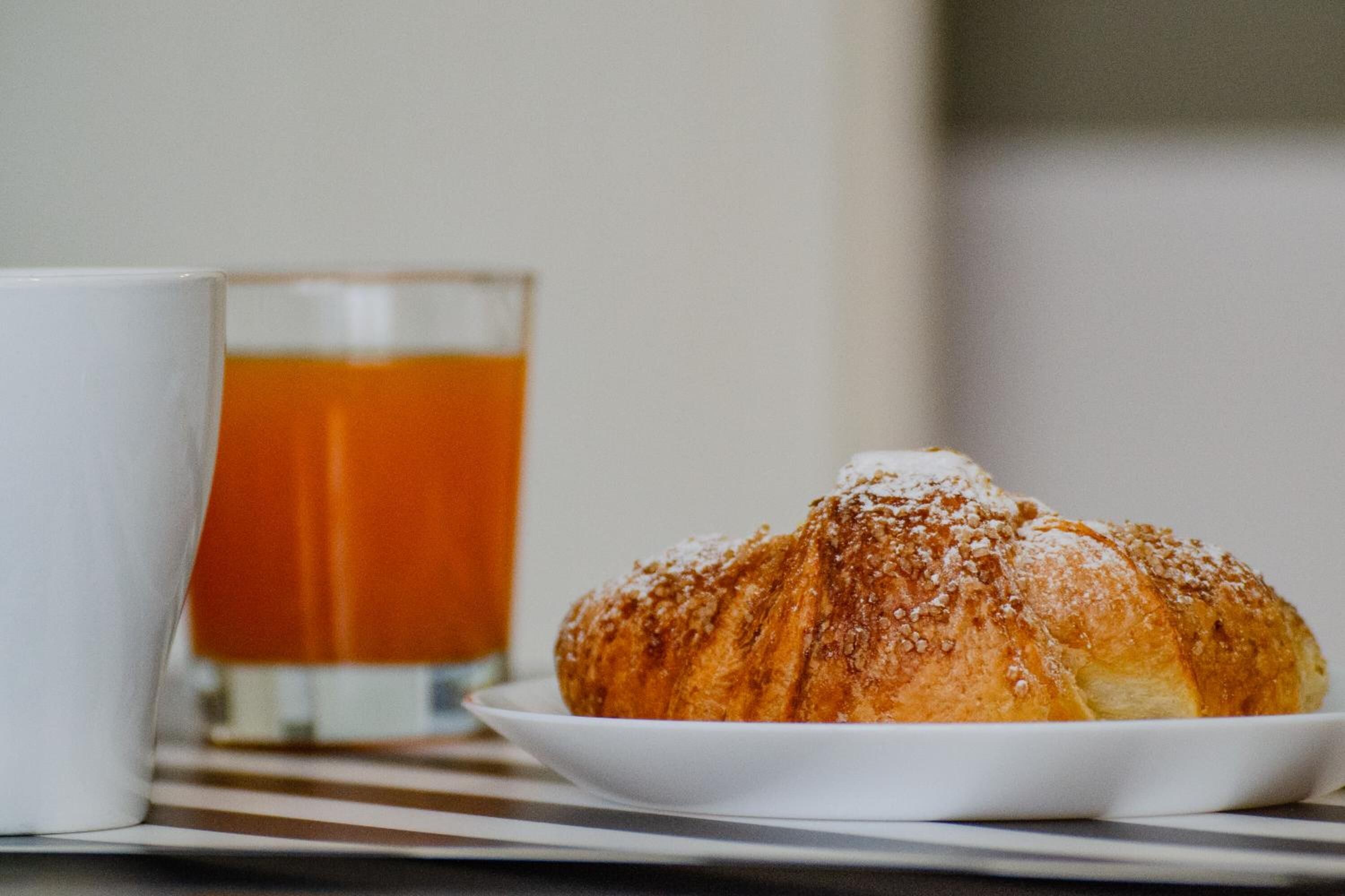 A croissant on a white plate with a glass of tea in the background.