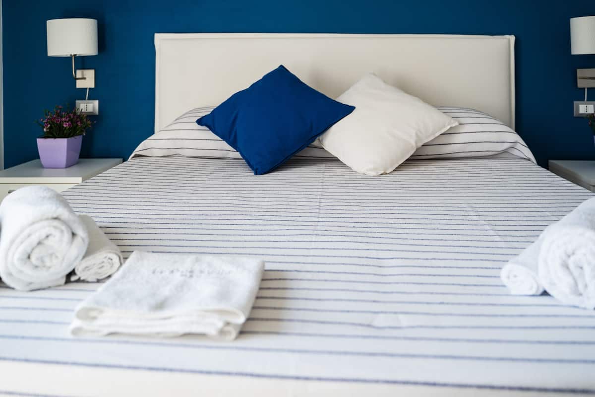 Ein ordentlich bezogenes Bett mit gestreifter Bettwäsche, einem blau-weißen Kopfkissen und aufgerollten weißen Handtüchern daneben.