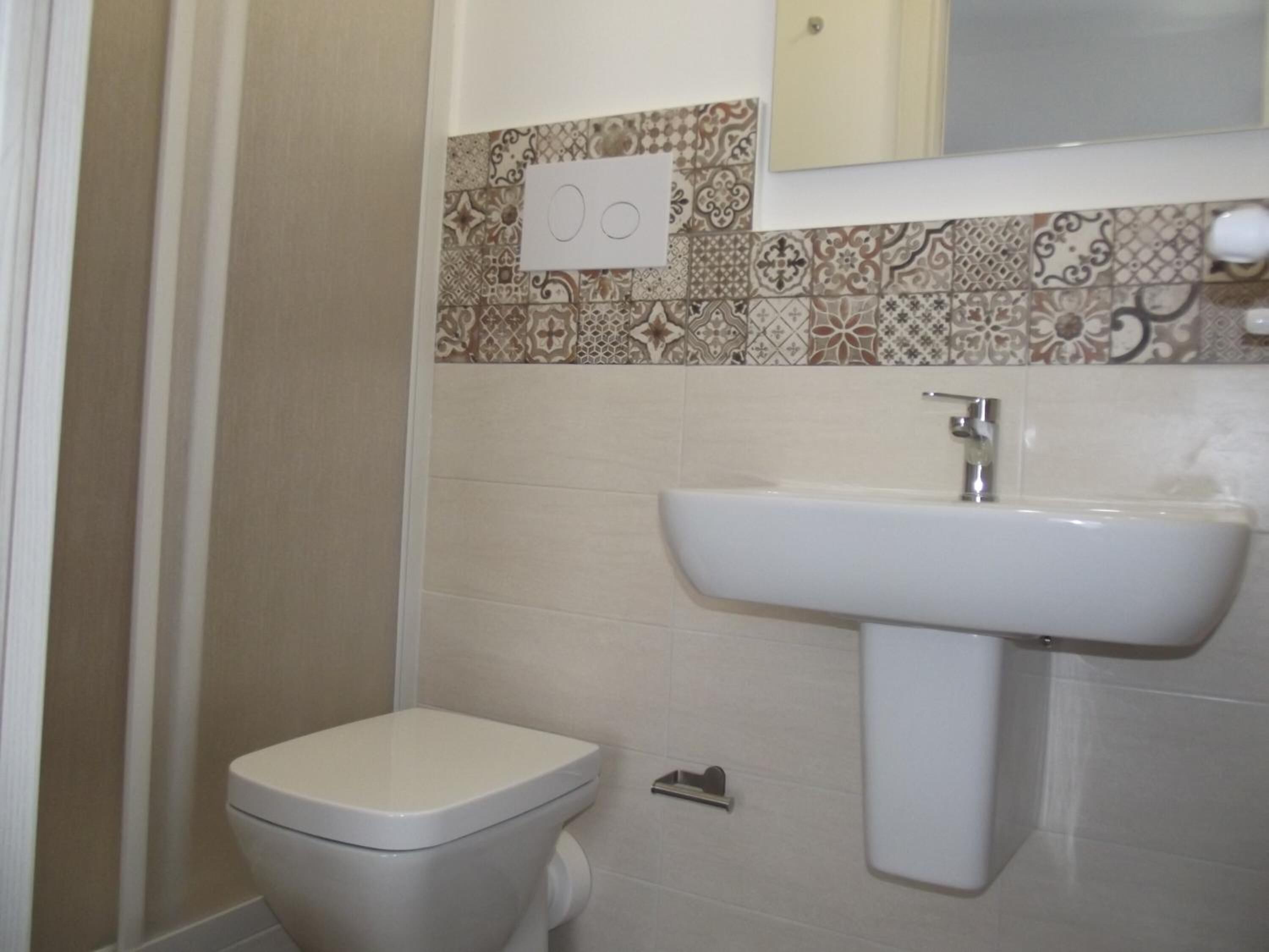 A bathroom with a toilet, a sink, and a patterned backsplash.