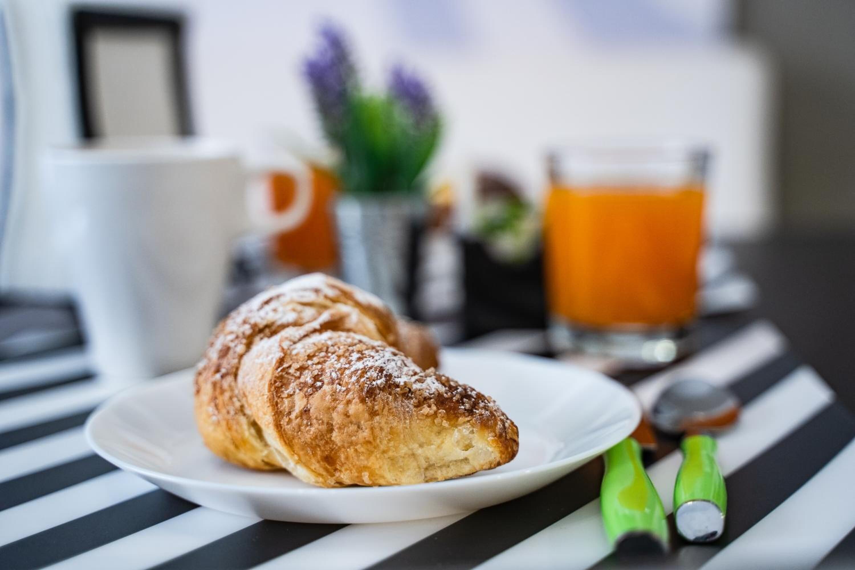 Een croissant op een wit bord, een glas sinaasappelsap en een geruit tafelkleed.