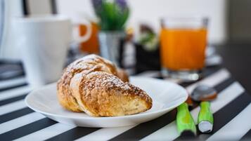 Een croissant op een wit bord, een glas sinaasappelsap en een geruit tafelkleed.