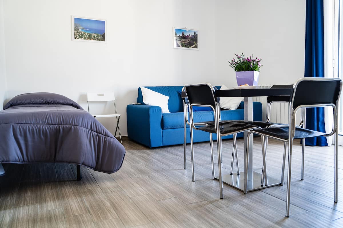Ein modernes Hotelzimmer mit einem Bett, einem blauen Sofa, einem Esstisch mit Stühlen und einer Topfpflanze.