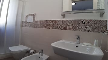 Un baño con inodoro, bidé, lavamanos y un espejo sobre el lavabo.