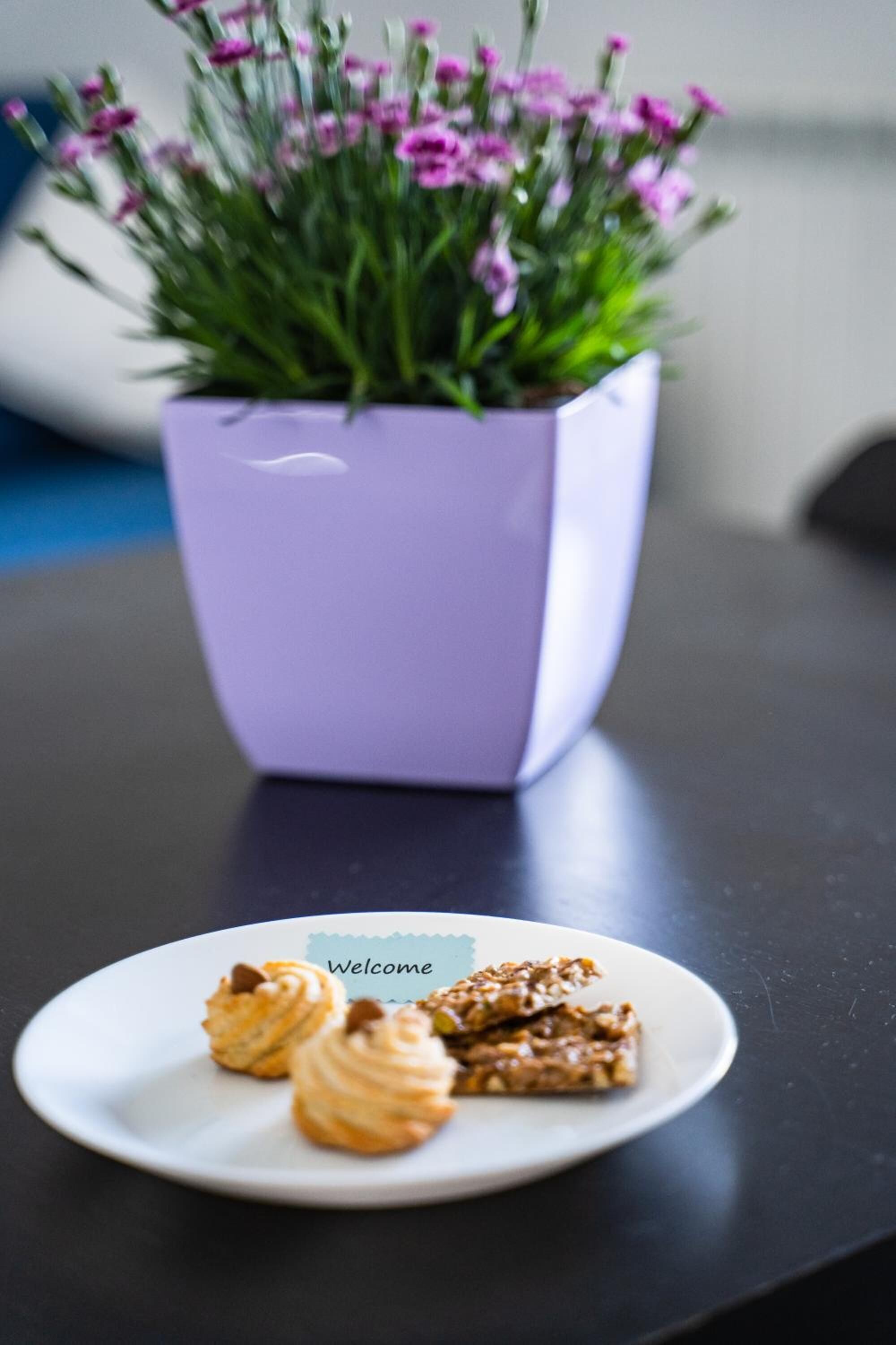 Une table avec un pot de fleurs violet et une assiette de pâtisseries.