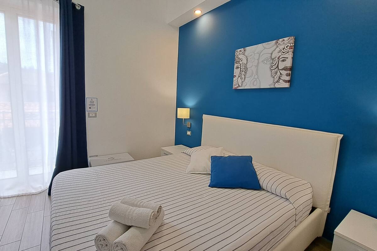 Ein Hotelzimmer mit einem großen Bett, zwei Kissen, einem Nachttisch, einer Lampe und einem Bild an der Wand.