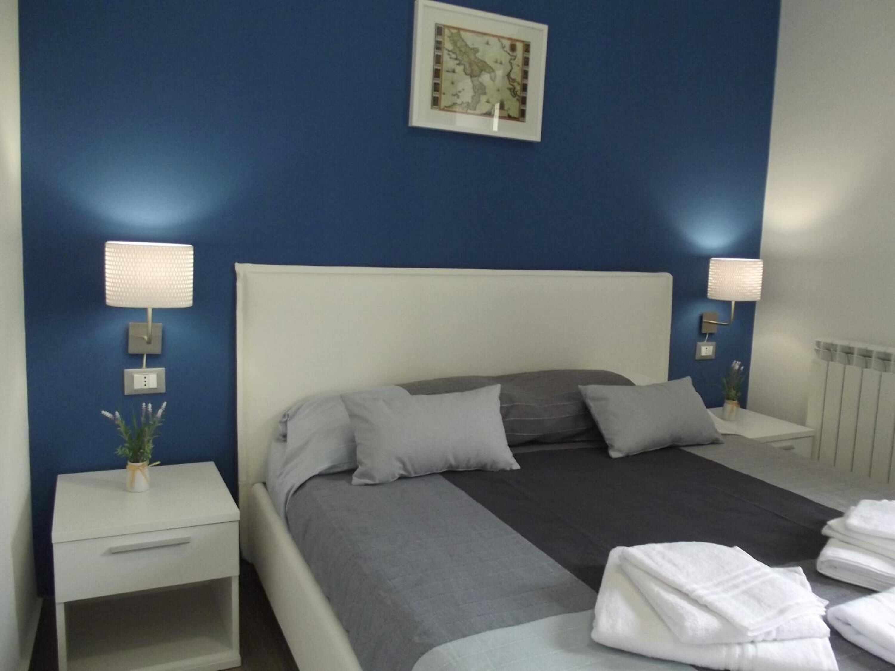 A neatly made bed with grey and white bedding, two bedside tables with lamps, and a framed map on the wall.