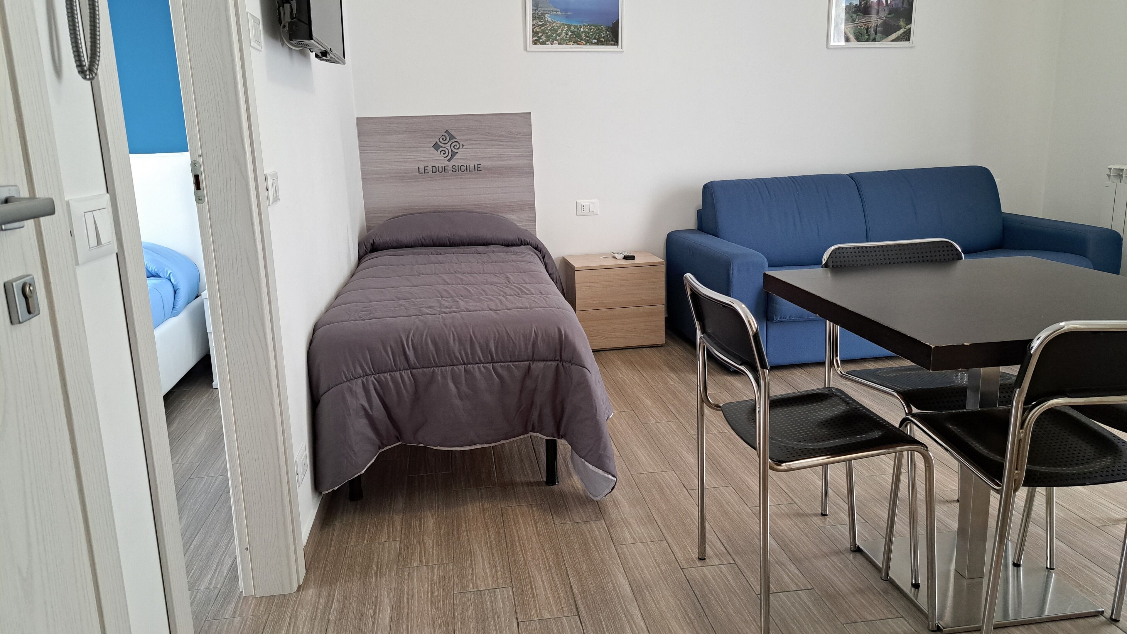 Una habitación pequeña con cama, sofá azul, una mesita y una silla.