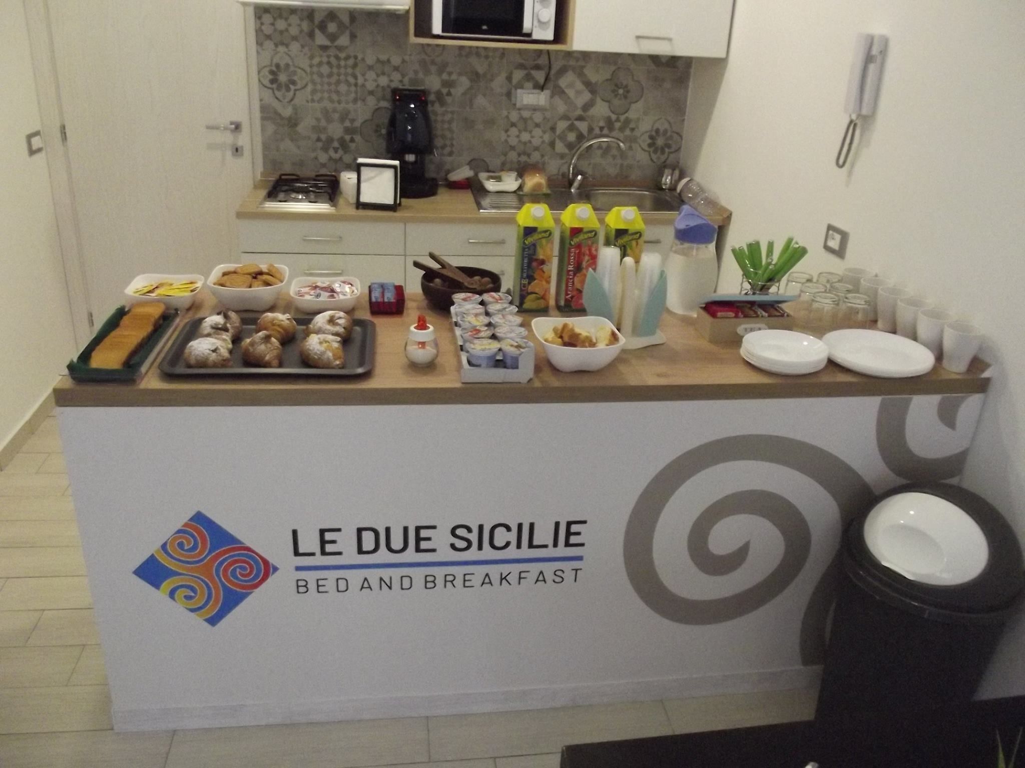 Ein Frühstücksbuffet mit verschiedenen Speisen und Beilagen, einer Kaffeemaschine und einer Mikrowelle darüber.