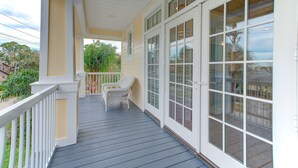 Une véranda couverte avec une balustrade blanche, une chaise en osier et de grandes fenêtres.