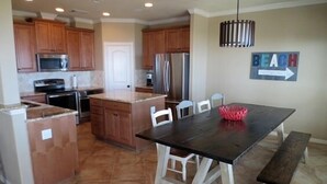A kitchen with wooden cabinets, a stainless steel refrigerator, and a dining table with chairs. - "As Good As It Gets" Beautiful Beach Front House! (Surfside Beach)