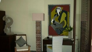 A room with a chair, a desk, a lamp, a decorative pillar, and a painting.