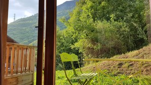 Una terraza de madera con vistas a una ladera verde exuberante y una montaña al fondo.