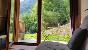 Una habitación con un ventanal grande, una terraza de madera, una pequeña mesa con sillas y un farol rojo en el exterior.