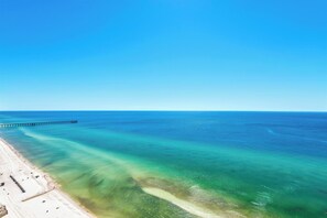 Una playa con aguas turquesas cristalinas, una orilla arenosa y un muelle que se adentra en el mar.