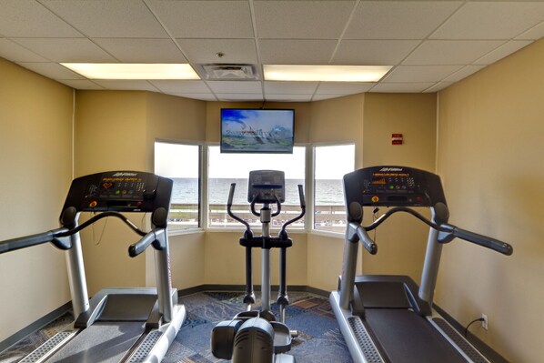 Un gimnasio con cintas de correr, un televisor y vista al mar.