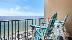 Un balcó amb dues cadires Adirondack turquesa, amb vista a una platja plena d'ombrel·les i persones.