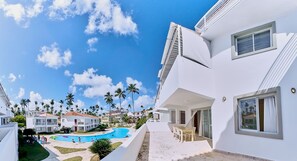 A modern building with a swimming pool, surrounded by palm trees and other buildings. - Los Corales Beach Village - Your private paradise - 2BR first floor - LT#D2b2 (Bávaro)