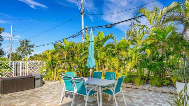 Eine Terrasse mit Tisch und Stühlen, umgeben von Palmen und einem Zaun.