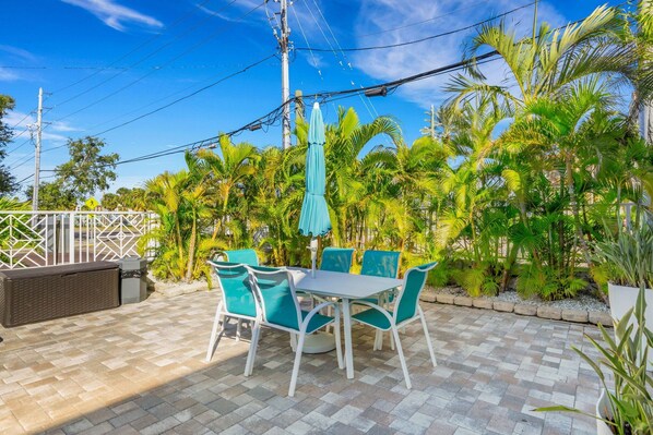 A patio with a table and chairs, surrounded by palm trees and a fence. - 🌴 Ground Floor Condo @ Clearwater Beach Suites | Steps to Sand • Heated Pool ➠ CBS 102 (Clearwater)
