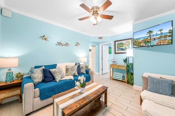 Settle into the cheerful coastal living room with comfortable seating, a sofa sleeper, ceiling fan, and wall-mounted TV.