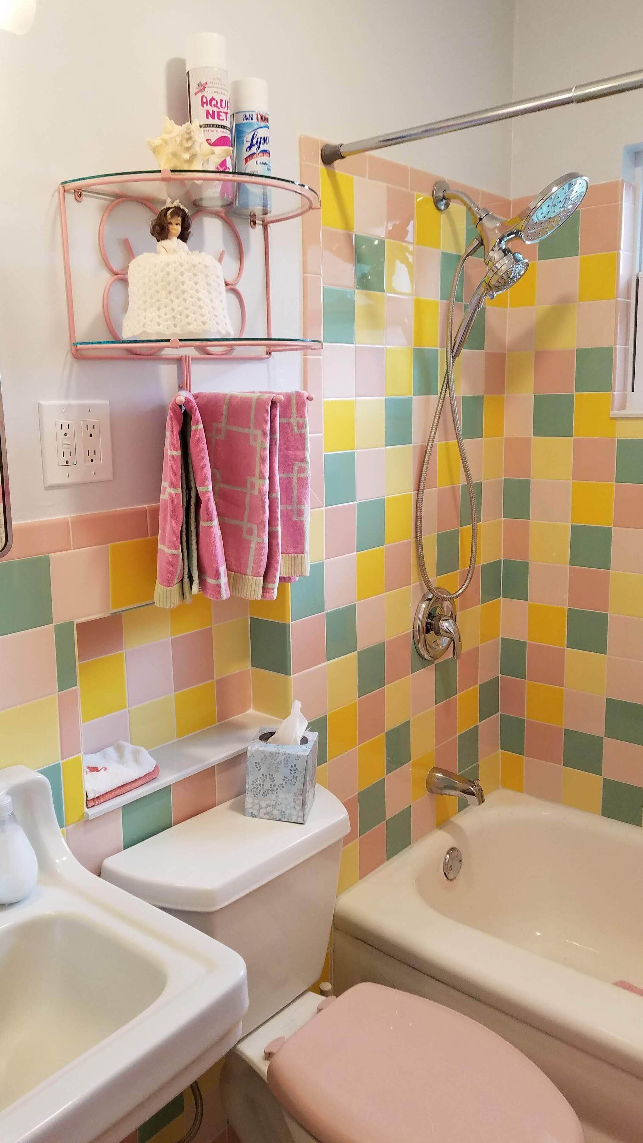 A bathroom with a toilet, bidet, and bathtub. There are colorful tiles on the walls, a glass shelf with toiletries, and a pink towel.