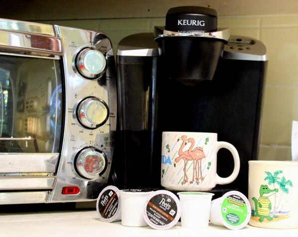A coffee maker, a mug with a flamingo design, and several coffee pods on a kitchen counter.