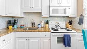A kitchen with white cabinets, a granite countertop, a white stove, and a microwave.