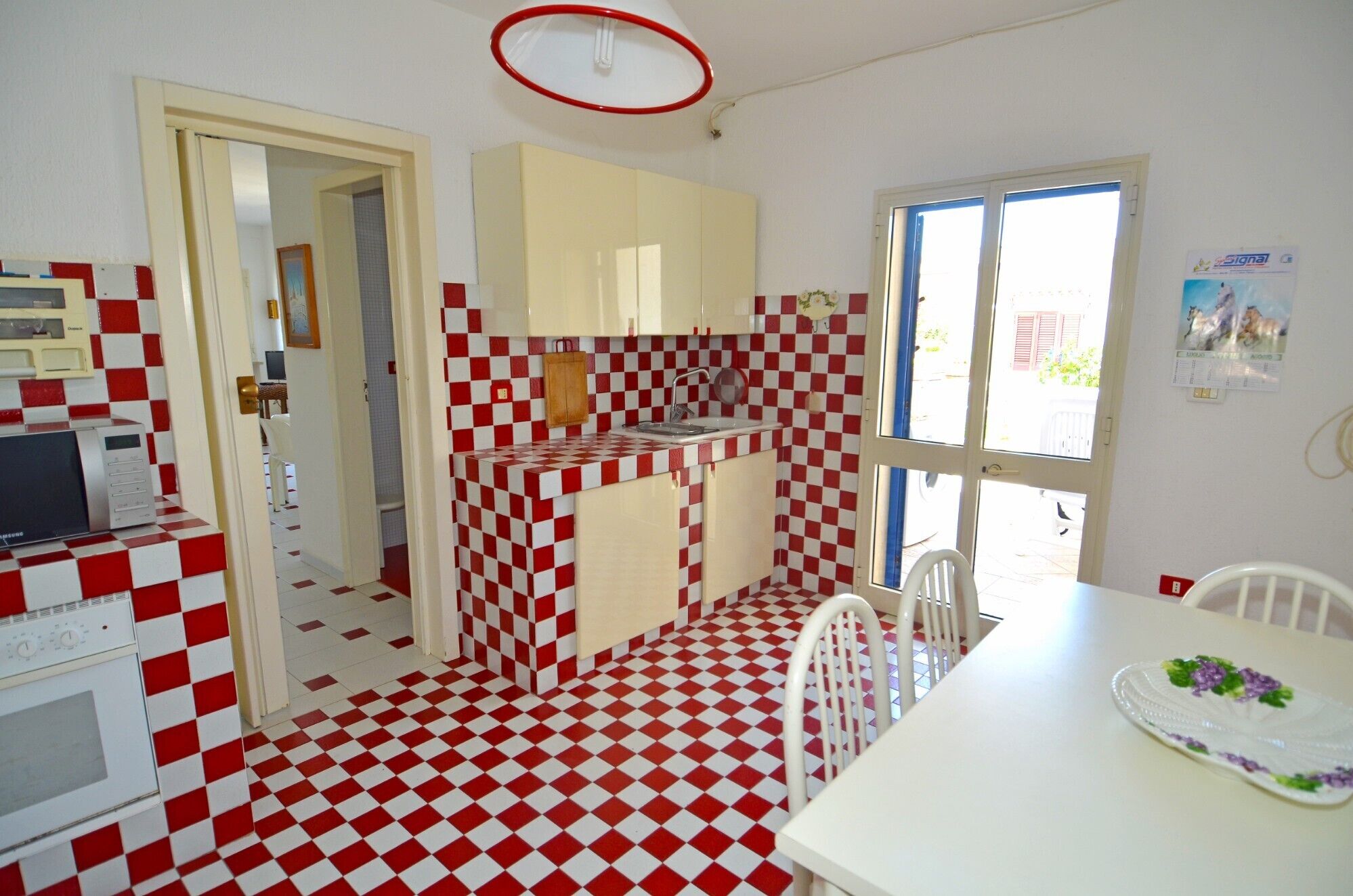 Uma cozinha compacta com chão quadriculado em vermelho e branco, uma pia pequena e eletrodomésticos básicos.