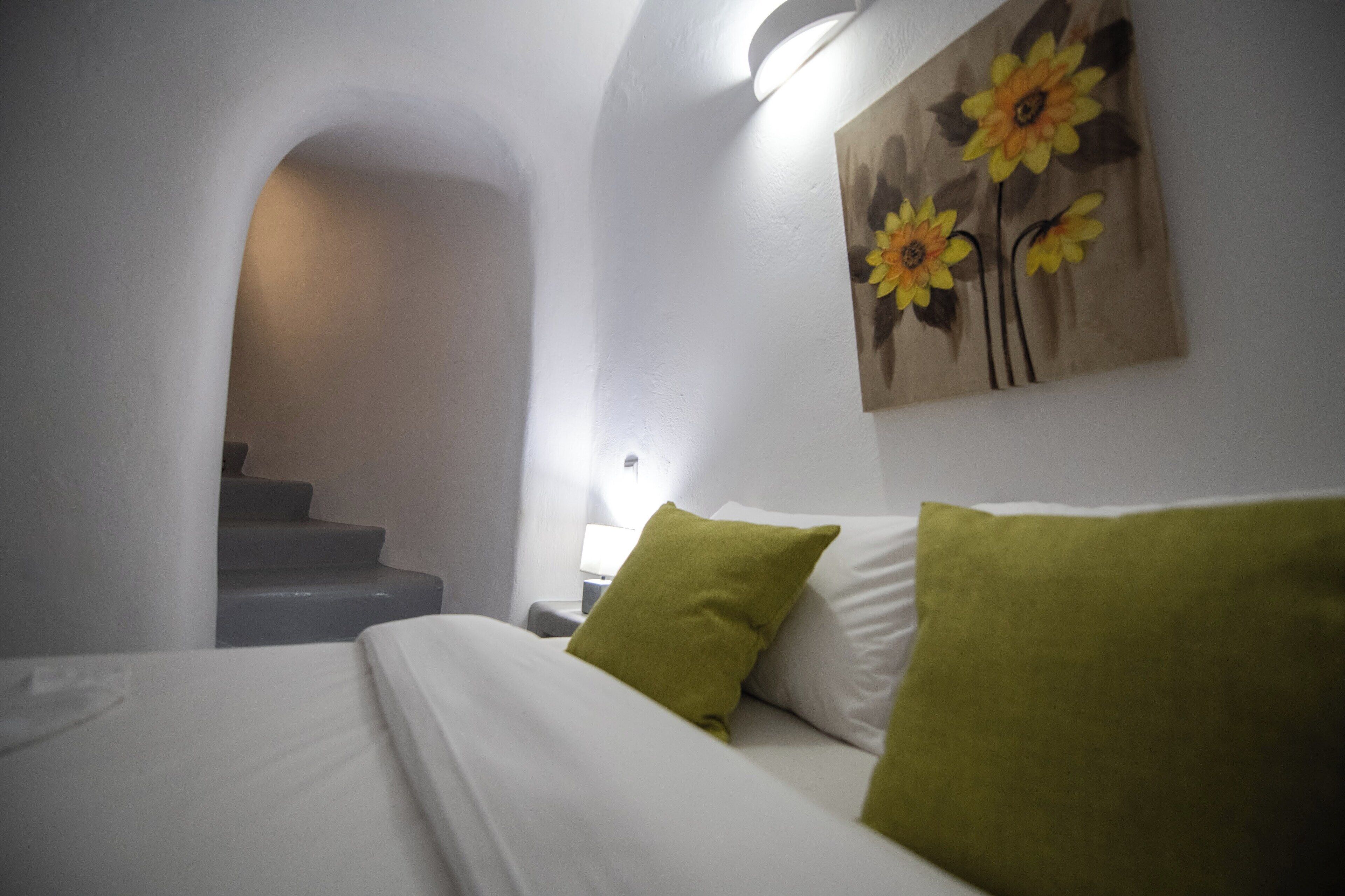 A hotel room with a bed, green pillows, a nightstand, a lamp, and a painting of sunflowers on the wall.