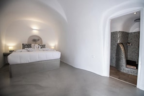 A bedroom with a large bed, a nightstand, a wall-mounted light, and a shower area with tiled walls.